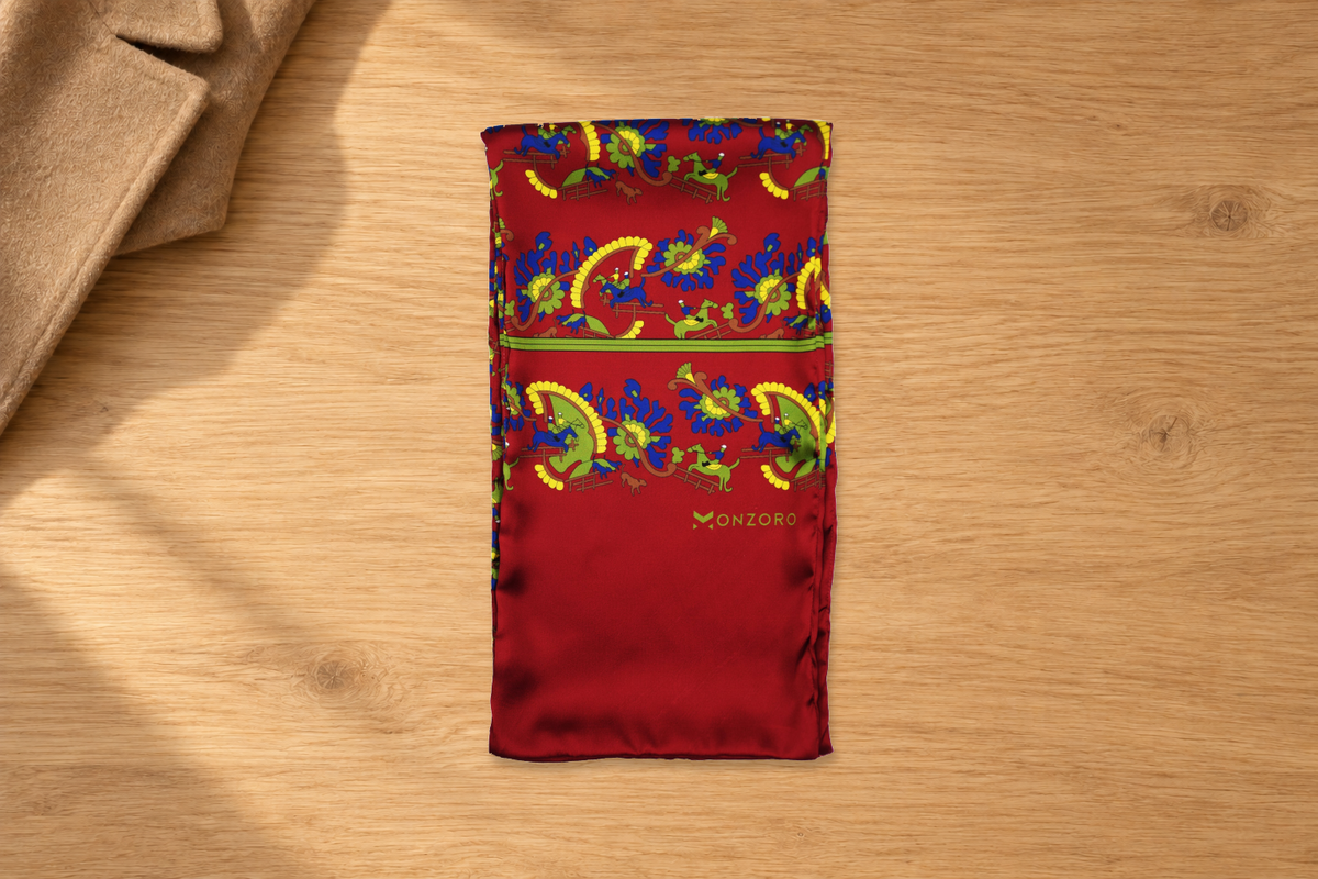 Folded maroon silk scarf with blue, green and yellow motifs beside camel wool on a pale wood dressing table.