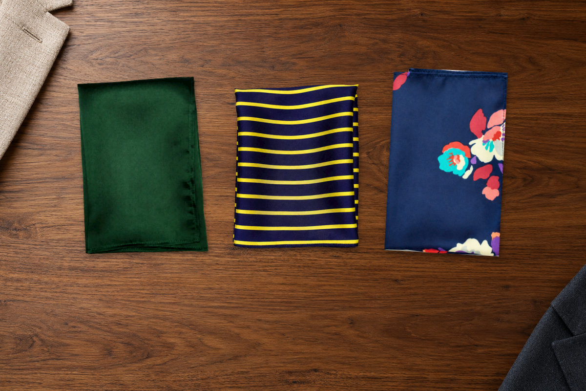 Deep green solid, blue-and-gold striped and navy floral pocket squares arranged on walnut.