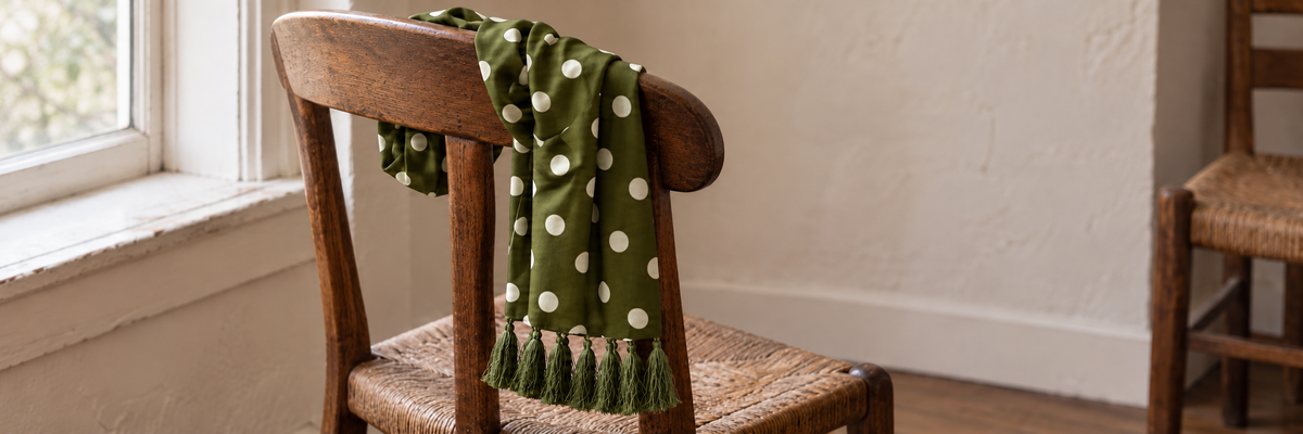 Olive polka-dot scarf draped naturally over an oak chair beside a window.