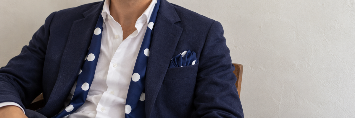 Seated wearer in a navy jacket with a matching navy polka-dot scarf and pocket square.