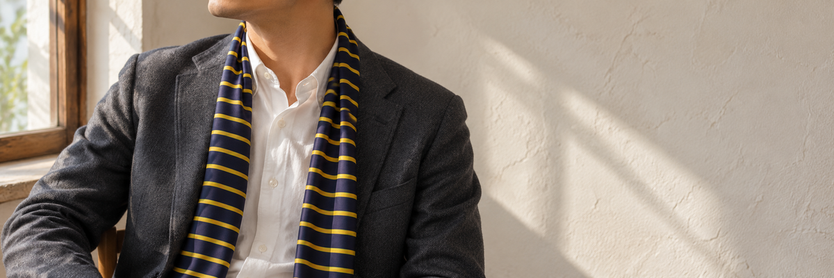 Blue-and-gold striped scarf worn naturally with a charcoal jacket beside a window.